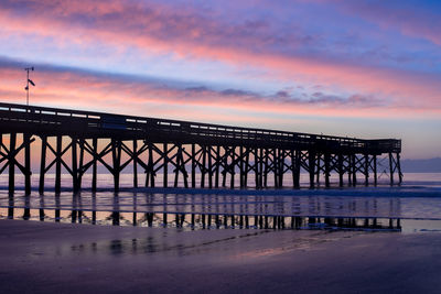 Silhouette bridge over sea against sky during sunset