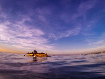 Man sitting in boat on sea against sky during sunset