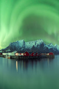 Spectacular view of vivid green polar lights shining in sky over residential houses located in highlands near lake in norway at night