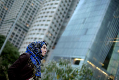 Side view of young woman standing against building in city