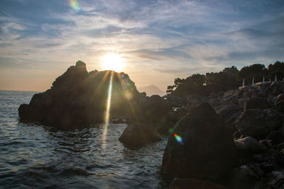 Rocks by sea against sky during sunset