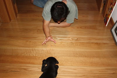 High angle view of man playing with black labrador puppy on hardwood floor at home