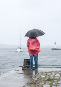 Rear view of woman with umbrella standing by sea during rainfall