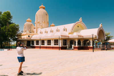 Rear view of woman standing by building against sky