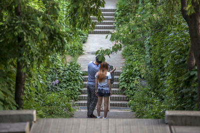 Rear view of man and woman standing on pathway amidst trees at park