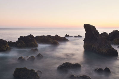 Scenic view of rock formations in sea against sky during sunset