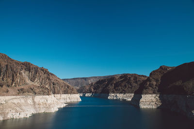 Colorado river amidst mountain at hoover dam against clear blue sky