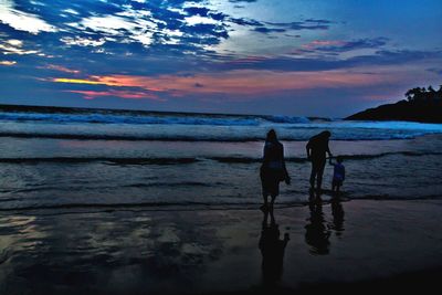 Silhouette people on beach against sky during sunset