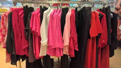 Various colorful clothes hanging on rack for sale at store