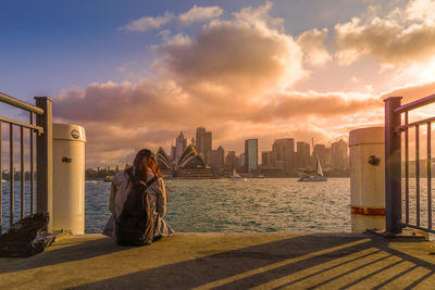 Woman by buildings against sky during sunset