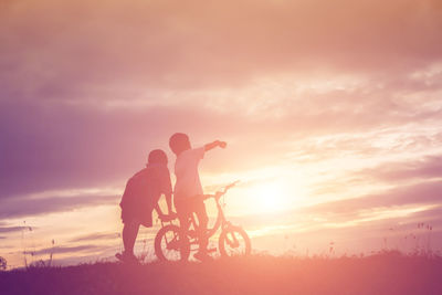 Silhouette man riding bicycle on field against sky during sunset