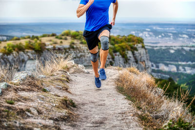 Male runner in knee pads running on narrow mountain path