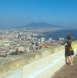 Woman standing by retaining wall and sea against buildings in city