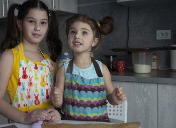 Portrait of curious sisters baking cookies at home