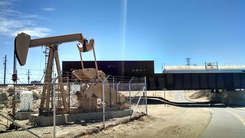 Oil machinery by freight train against sky