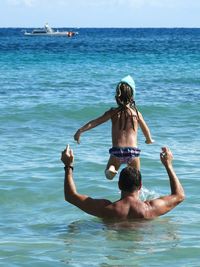 Rear view of father and daughter enjoying at beach against sky