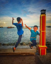 Siblings playing on pier against sky during sunset