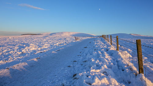 Snow covered landscape against clear blue sky