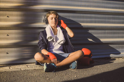 Full length of boy listening music while sitting on road