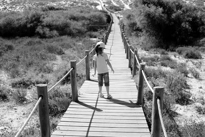 Rear view of girl walking on footbridge over field