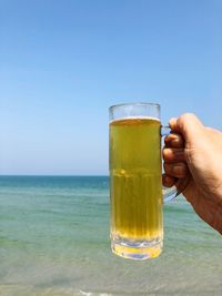 Close-up of hand holding beer glass against clear sky