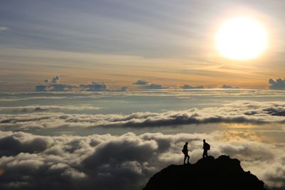 Silhouette friends standing on mountain during sunset