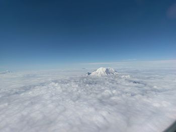 Snowcapped mountain amidst cloudscape against clear sky seen through airplane window