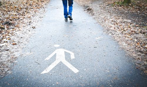 Low section of man walking on road with pedestrian sign