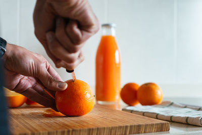 Cropped image of man holding orange on cutting board