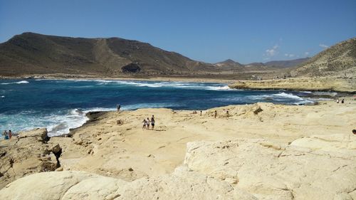 People standing on beach against clear blue sky