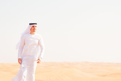 Man in traditional clothing standing on sand dune against sky