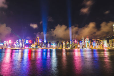 Illuminated city by river against sky at night