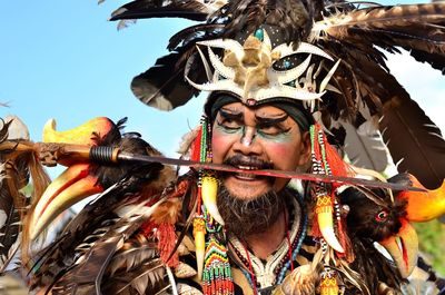 Man wearing native costume holding sward in mouth