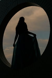 Silhouette of young woman in a blue dress against a clouded sky.