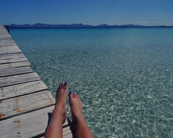 Low section of woman relaxing by sea against sky