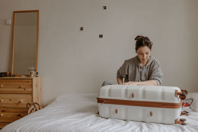 Smiling woman packing her suitcase at home on the white bed