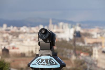 Close-up of coin-operated binoculars by townscape against sky