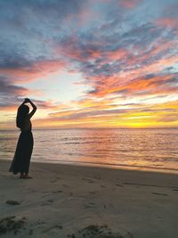 Rear view of woman standing on beach against sky during sunset