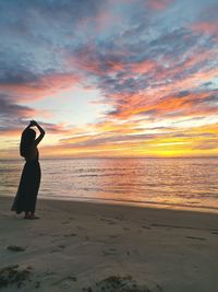 Woman standing at beach against sky during sunset