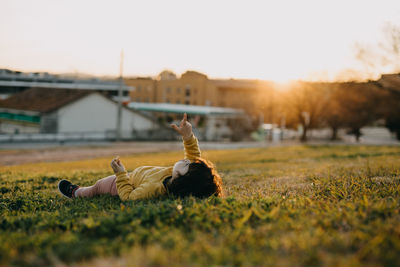 Child lying on field against sky