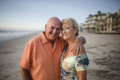 Portrait of smiling senior couple standing at beach against sky