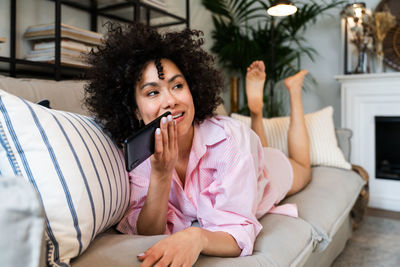 Young woman looking away while lying on sofa at home