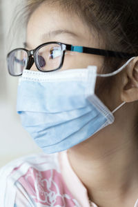 Close-up of girl wearing mask looking away sitting at home