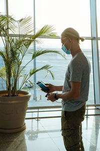 Man with power bank at the airport, charging phone passenger in mask traveling during covid. 