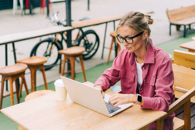 Young blonde business woman sitting on the terrace in a cafe working on a laptop.