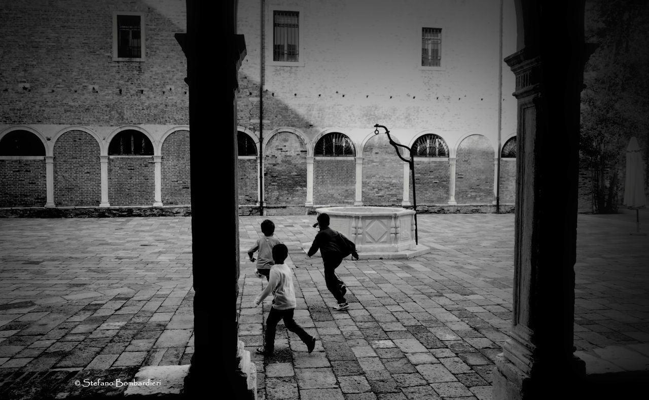 architecture, built structure, building exterior, men, lifestyles, walking, person, street, cobblestone, arch, rear view, city, full length, leisure activity, sidewalk, city life, umbrella