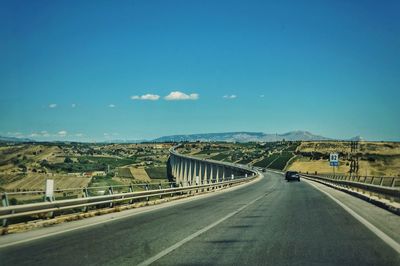 Road leading towards mountains against blue sky