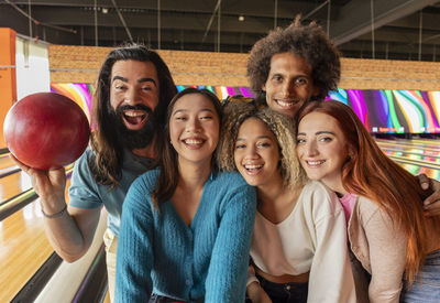 Happy young women with men standing together at bowling alley