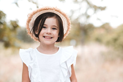 Cute smiling baby girl wearing straw hat and short cut hair pose outdoors over nature background