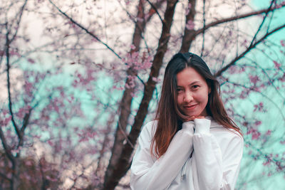 Portrait of smiling young woman standing by flower tree